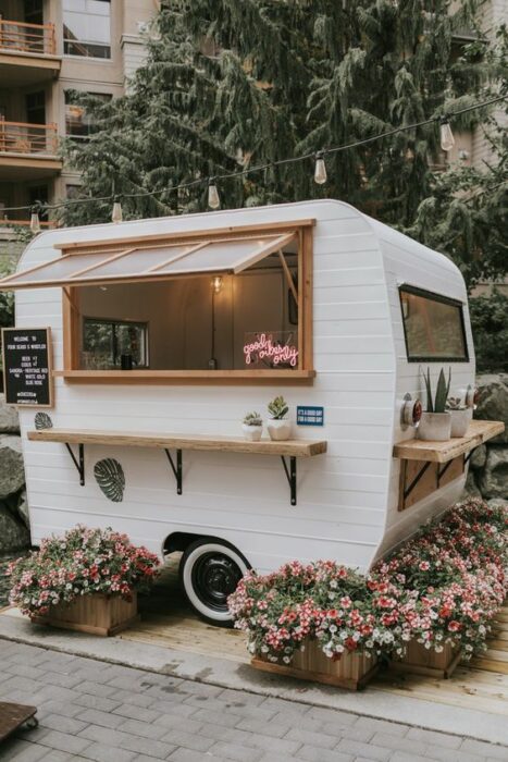 Mini Van de comida en color blanco con detalles cafés rodeada de flores rosas