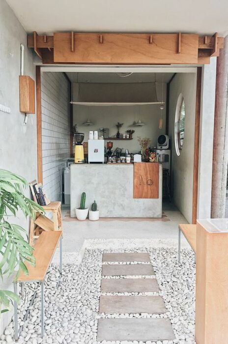 Mini restaurante en material de concreto con mesas y detalles de madera con decoración de plantas y cactus  