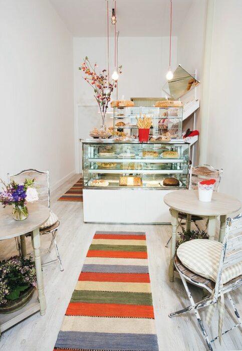 Cafetería blanca con mesa redondas beige con tapete de colores que va directo a la vitrina transparente 