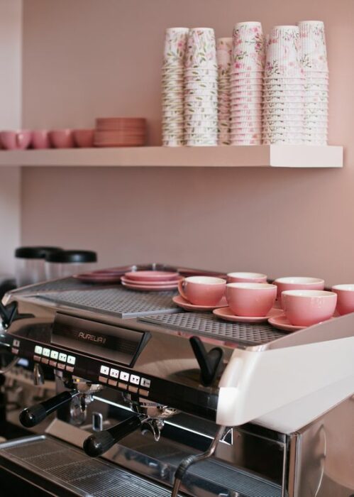 Cafetería de paredes rosas con platos y tazas rosa y maquina de café plateada