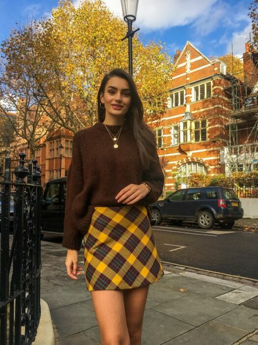 Chica con minifalda a cuadros amarillos, suéter café; ideas para usar minifalda con suéter en otoño-invierno