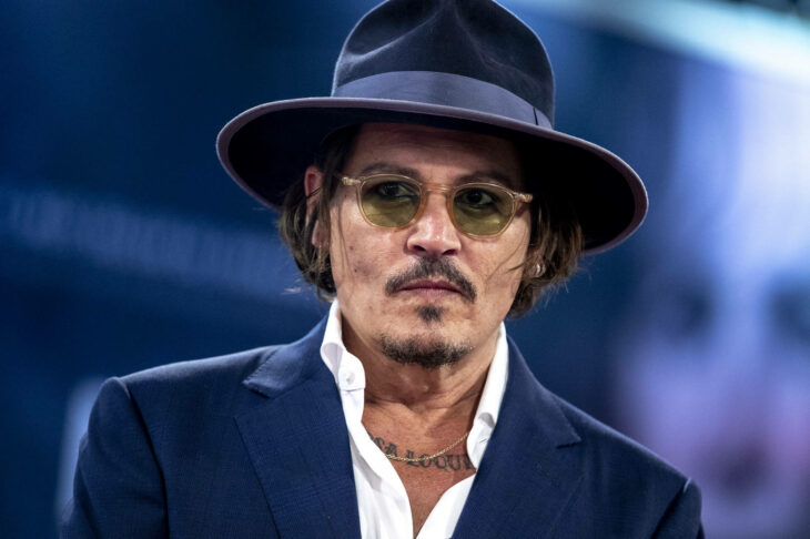 Actor Johnny Deep usando camisa blanca, saco y sobrero con unos lentes de sol