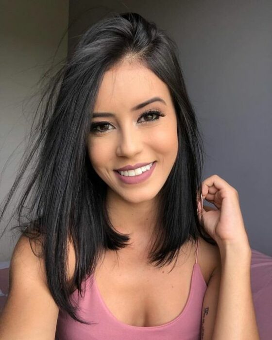 Chica morena sonriente con cabello larcio y negra con blusa de tirantes blanca