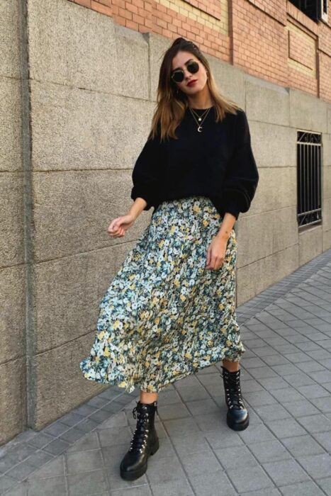 Chica usando un maxivestido de color verde con botines y un suéter de color negro 