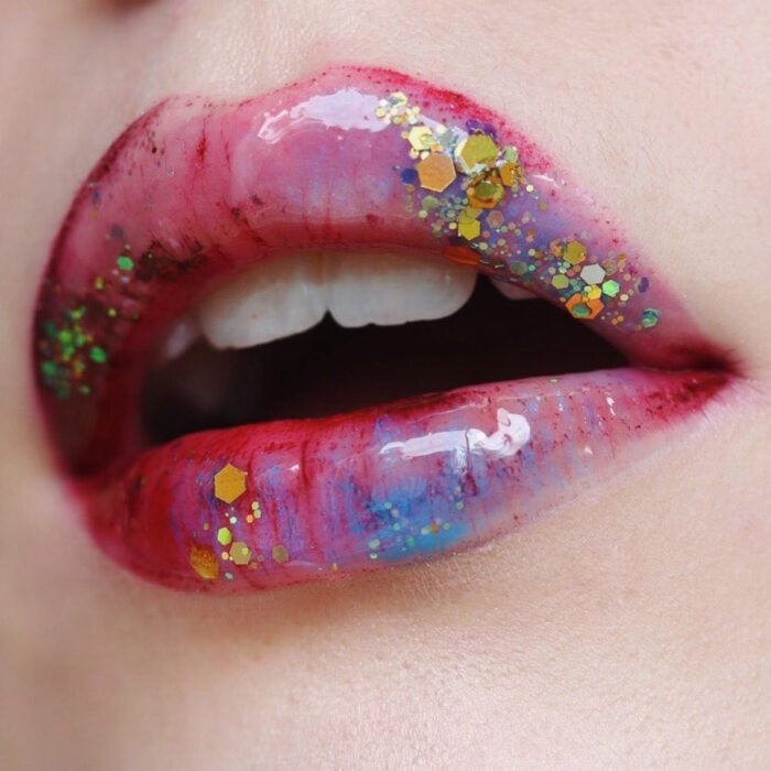 Künstlerisches Lippen Make-up von Maskenbildnerin Tatiana Rose;  Mund mit rosa, blauem und rotem Lippenstift mit goldenem und grünem Glitzer