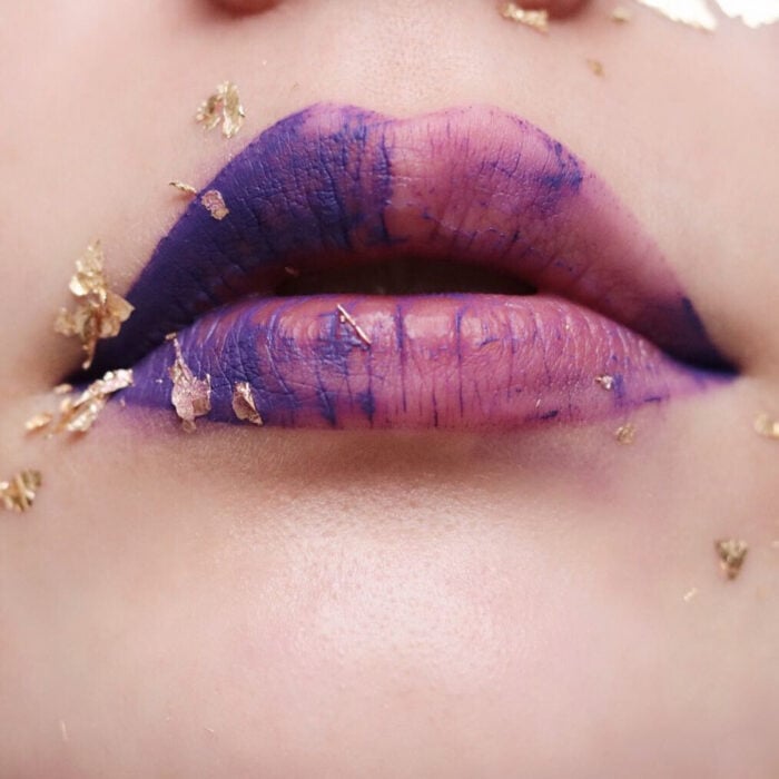 Maquillaje artístico de labios por maquilladora Tatiana Rose; boca con labial de dos colores, mitad morado y mitad rosa con láminas de oro