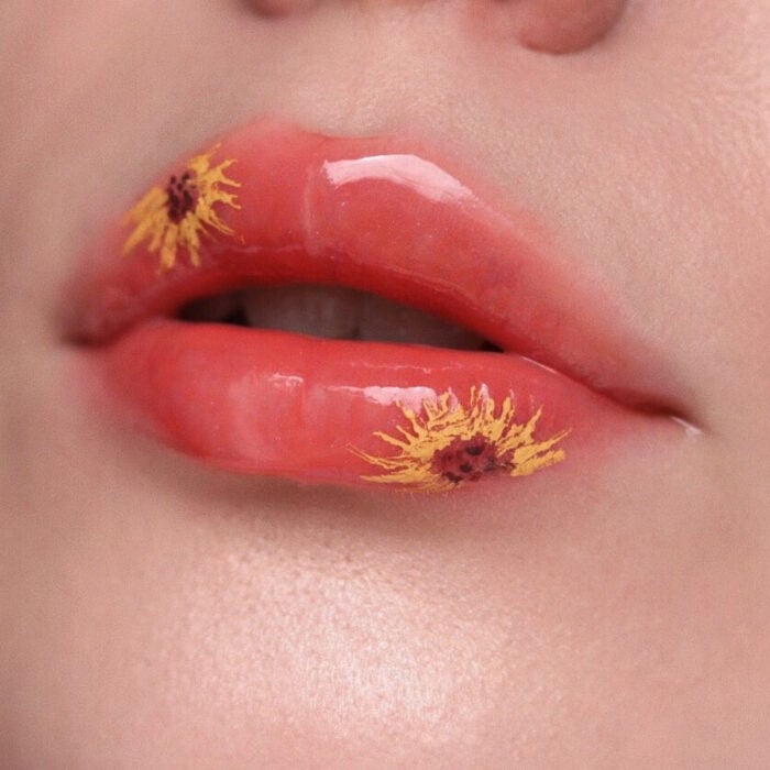 Künstlerisches Lippen Make-up von Maskenbildnerin Tatiana Rose;  Mund mit pfirsichrosa Lippenstift mit Sonnenblumenblumenzeichnungen, Glanz