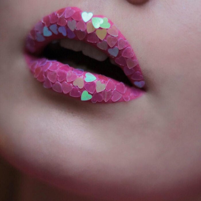 Künstlerisches Lippen Make-up von Maskenbildnerin Tatiana Rose;  Mund mit rosa Lippenstift und grünem, blauem und lila herzförmigem Glitzer
