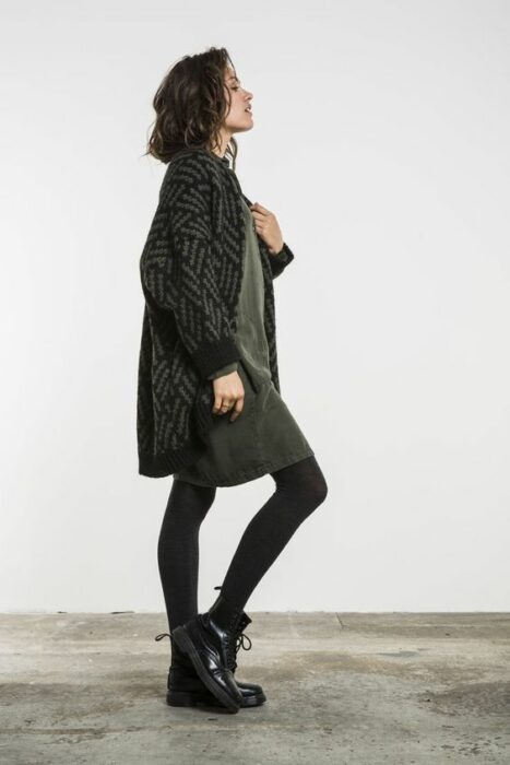 Chica usando botines, mayas negras y vestido color verde militar con cardigan largo negro con gris