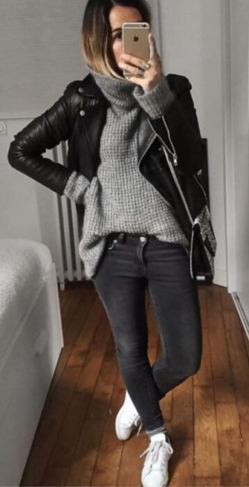 Chica usando jeans negros deslavados, tenis blancos, suéter gris olgado y chaqueta negra de cuero