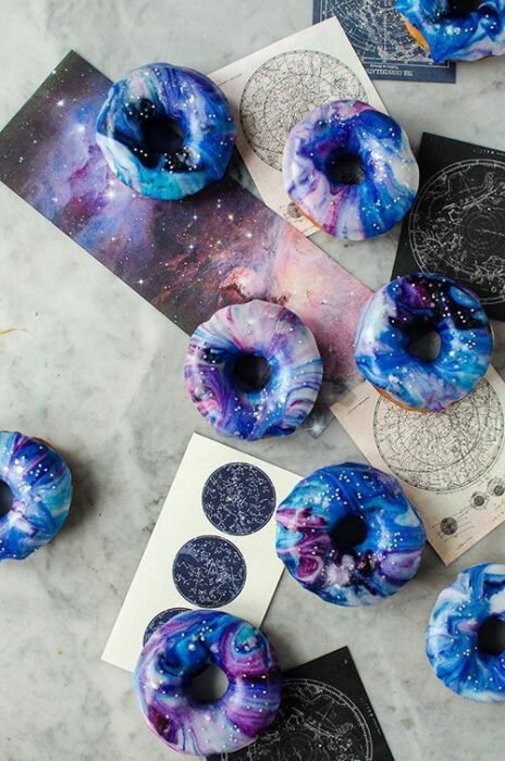 Rosquillas decoradas con betún en colores blanco y morados; Pasteles inspirados en la galaxia