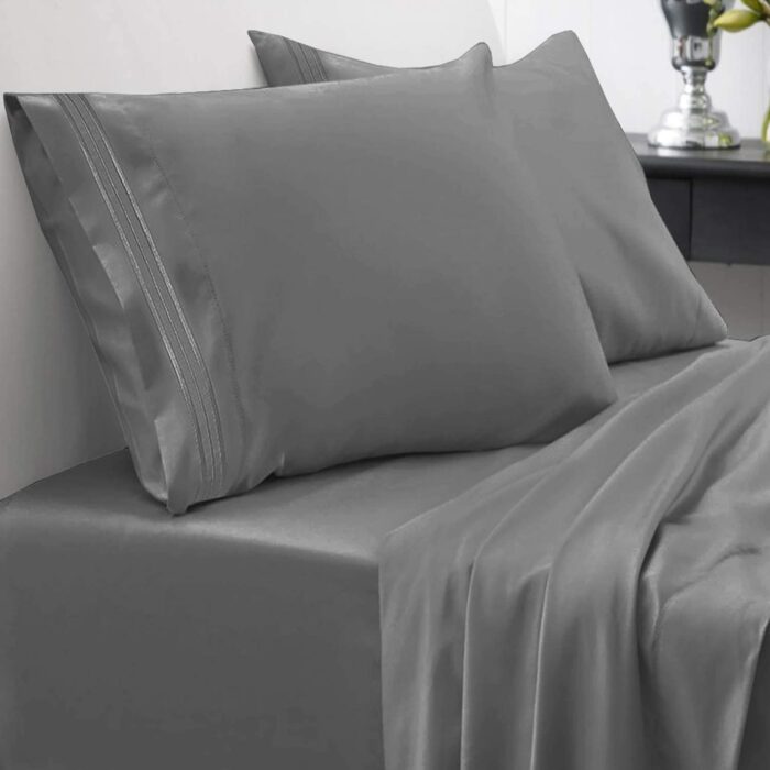 Cama cubierta con unas sabanas de color gris con almohadas y sabana de cajón