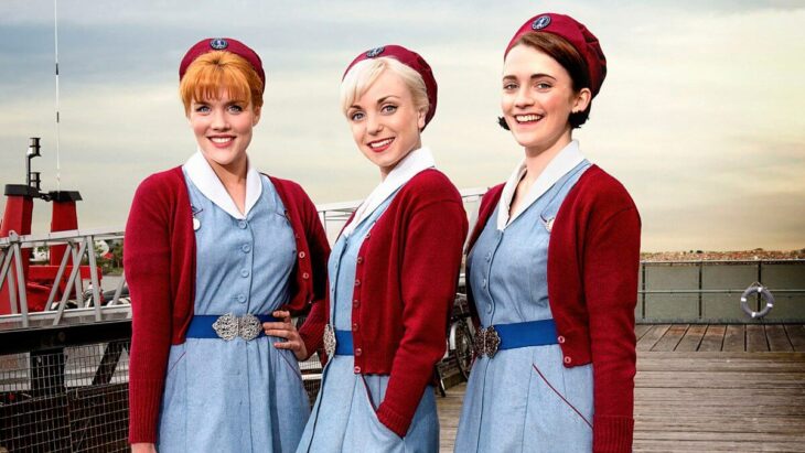 Escena de la serie Call the Midwife,trío de amigas llevando vestido azul y suéter rojo