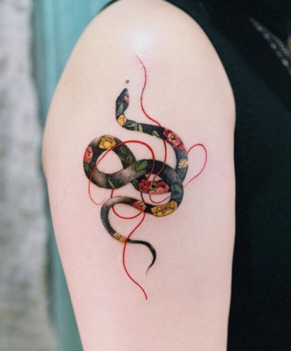Tatuaje de serpiente en tinta de varias colores y un hilo rojo sobre la zona del hombro