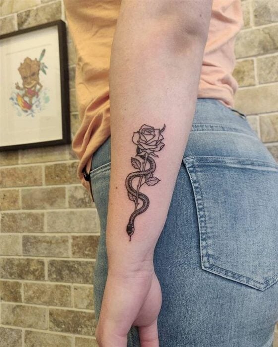 Tätowierung einer Schlange, die mit einer Rose in schwarzer Tinte auf dem Unterarm verschlungen ist