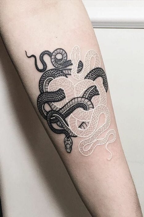 Tatuaje de dos serpientes entrelazadas en tinta blanco y negro sobre el antebrazo