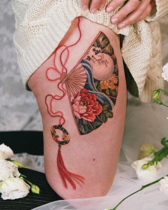 Tatuaje de abanico asiático en el brazo con colgante de hilo rojo