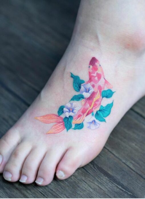 Tatuaje en el entre peine de pez koi con flores blancas y hojas verdes