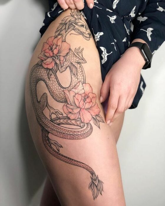 Tatuaje de dragón en tinta negra con flores de cerezo en la pierna de una mujer