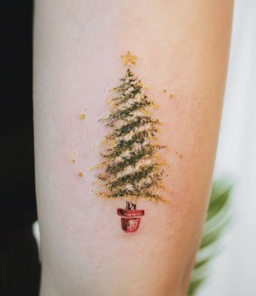Chica llevando tatuaje en forma de pino con estrella amarilla; Tatuajes para las chicas que aman Navidad