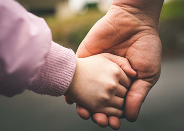 Mano de hombre sujetando a manita de una niña con suéter rosa