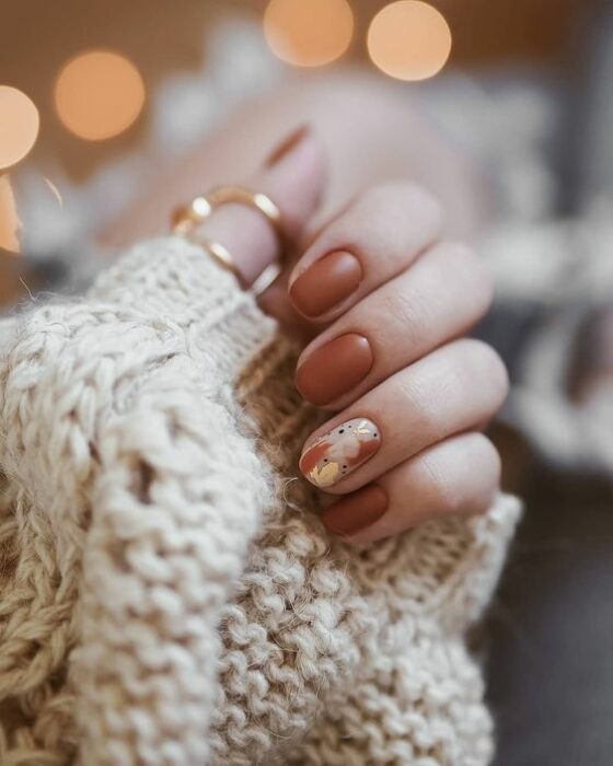 Manicura natural en tono café con detalles en blanco y naranja en dedo anular