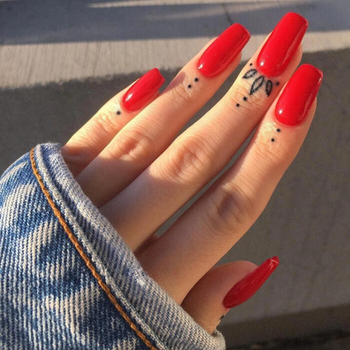 Manos bonitas de mujer con manicura, uñas largas cuadradas con esmalte de color rojo, dedos con tatuajes tribales de puntos y flores