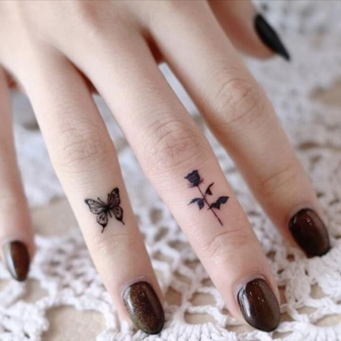 Manos bonitas de mujer con manicura, uñas cortas redondas con esmalte color café con brillos, dedos con tatuajes de mariposa y rosa