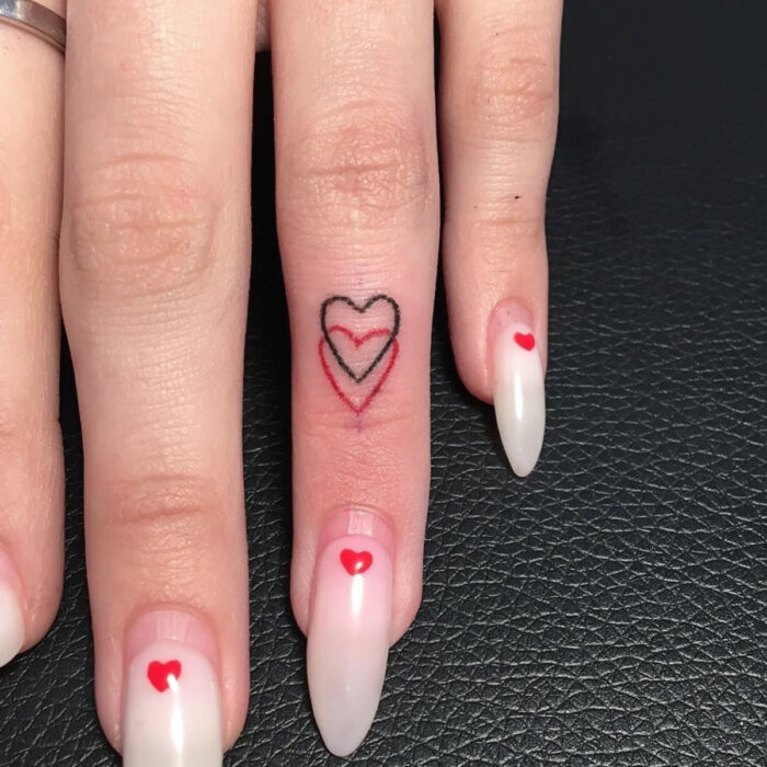 Manos bonitas de mujer con manicura, uñas largas stiletto con esmalte blanco mármol con diseño de corazón, dedo con tatuaje de corazones negro y rojo