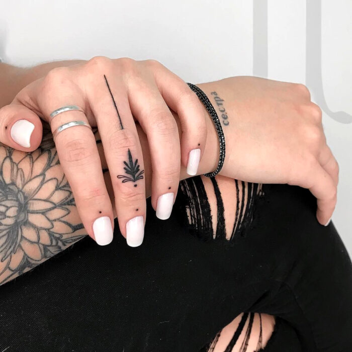 Manos bonitas de mujer con manicura, uñas cortas cuadradas con esmalte color blanco, dedos con tatuajes minimalistas de planta, puntos y línea, anillos plateados