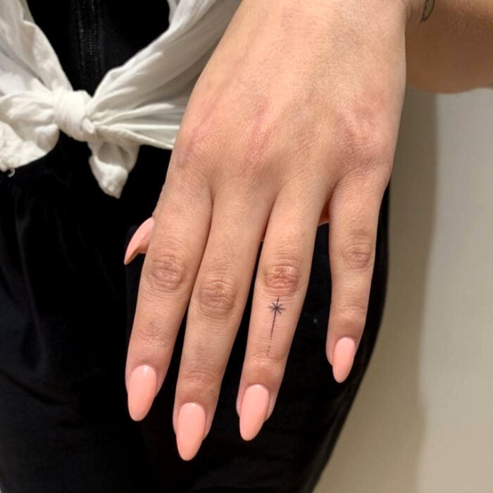Hübsche Frauenhände mit Maniküre, langen mandelförmigen Nägeln, nackter Farbe, Pfirsichrosa, Sternschnuppen-Tätowierung auf Mittelfinger