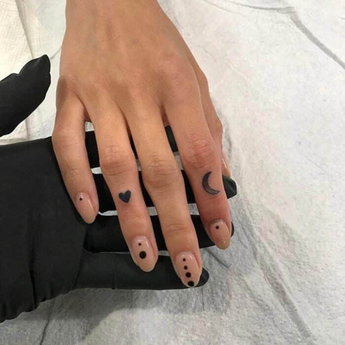 Manos bonitas de mujer con manicura, uñas cortas redondas con esmalte color nude con diseño de puntos, dedos con tatuajes de corazón y Luna