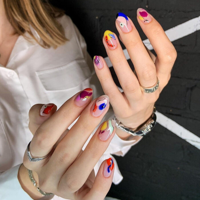 Diseños bonitos de manicura coloridos; manos de mujer con uñas largas en forma de almendra pintadas con esmalte de diferentes formas con diseños abstractos, azul, nude, rosa, amarillo, lila, rojo, anaranjado y verde menta