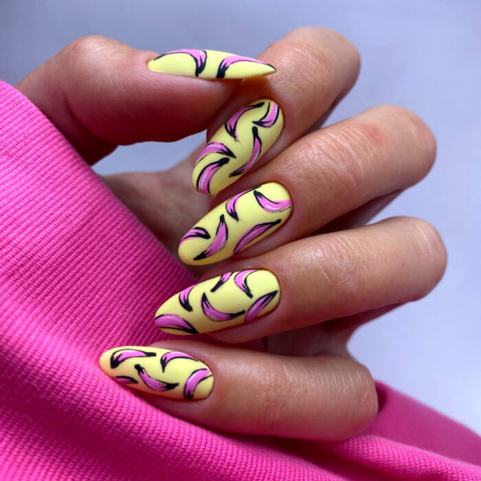 Diseños bonitos de manicura coloridos; mano de mujer con uñas largas en forma de almendra pintadas con esmalte amarillo y rosa con diseño pop art de plátanos