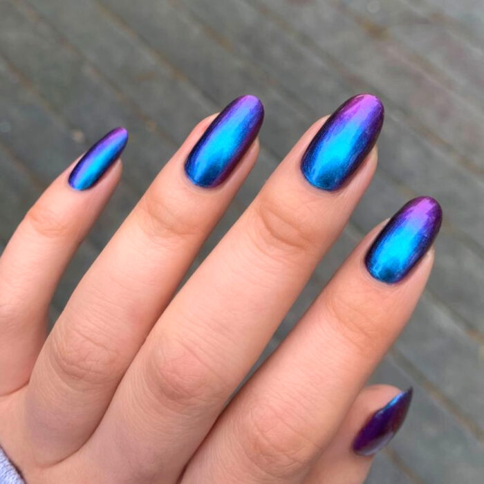 Diseños bonitos de manicura coloridos; mano de mujer con uñas largas en forma de almendra, pintadas con esmalte holográfico de colores morado y azul