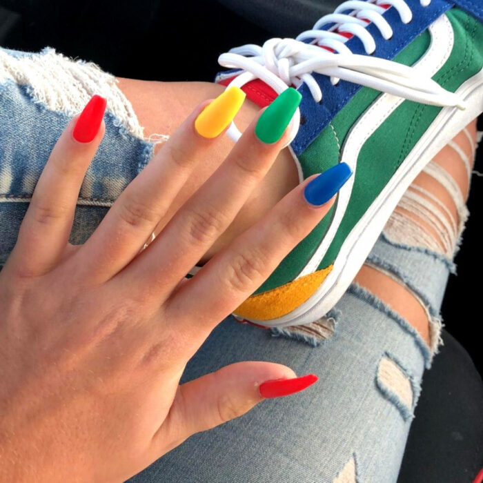 Diseños bonitos de manicura coloridos; uñas largas cuadradas de bailarina pintadas con esmalte mate de colores cada una, rojo, amarillo, verde y azul, tenis coloridos