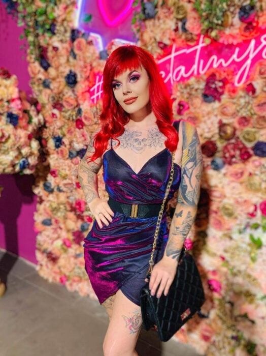 Vestido iridiscente, holográfico de tirantes con cinto ancho, mujer pelirroja, con tatuaje de calavera y flores en el pecho y brazos