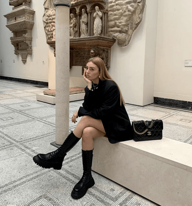 chica rubia usando un blazer negro oversized, botas de cuero de plataforma, bolso de mano negro