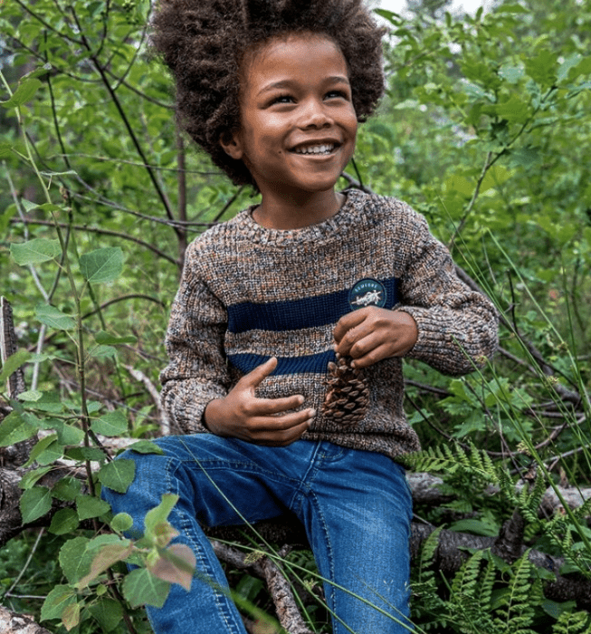 niño de cabello chino usando un suéter café tejido, pantalón de mezclilla azul