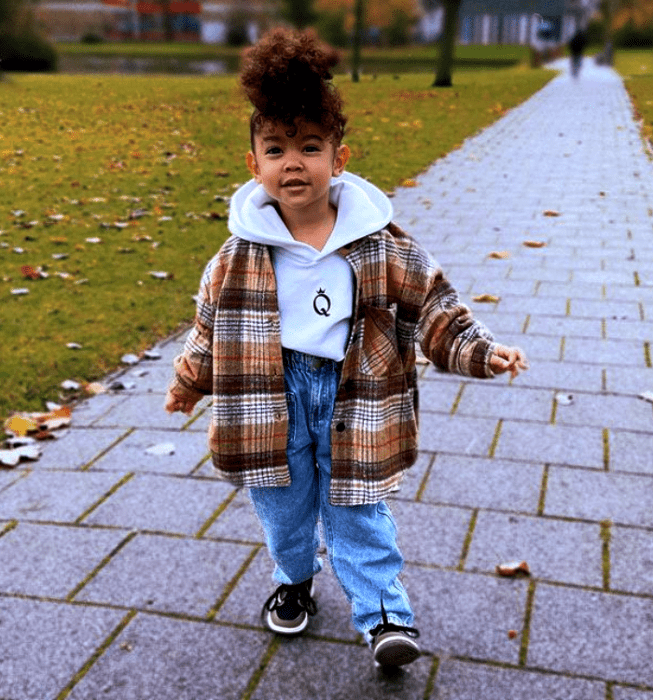 niña de cabello castaño chino usando una sudadera blanca, chamarra café de cuadros, pantalones de mezclilla, tenis negros con blanco