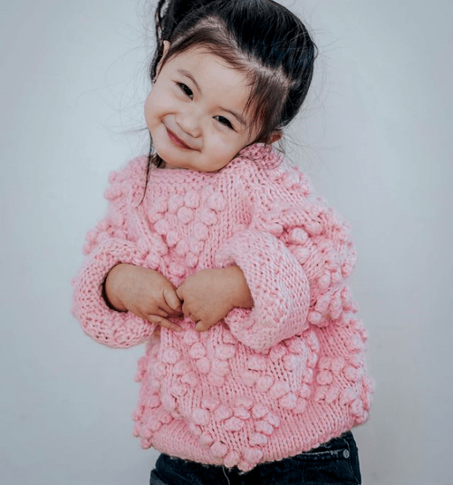 niña de cabello oscuro usando un suéter tejido rosa y shorts de mezclilla