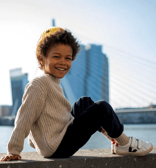 niño de cabello chino usando un suéter gris tejido, pantalones azules, tenis blancos