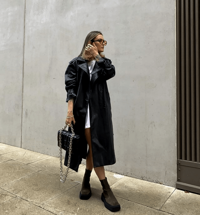 chica rubia con lentes de sol, vestido mini blanco, abrigo largo de cuero, botas de suela gruesa, bolso de mano de cuero color negro