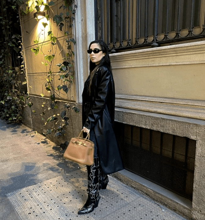 chica de cabello negro usando lentes de sol, abrigo de cuero largo, botas largas de cuero con tacón, bolso de mano beige