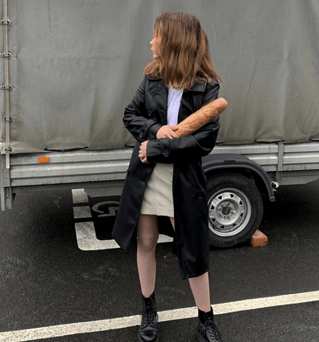 chica de cabello claro usando una camiseta blanca, minifalda beige, abrigo largo de cuero y botas de suela gruesa negras