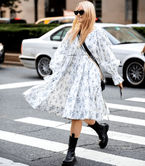 chica rubia usando un vestido largo blanco con mangas abombadas, con flores azules pequeñas, botas negras de suela gruesa y bolso negro crossbody bag