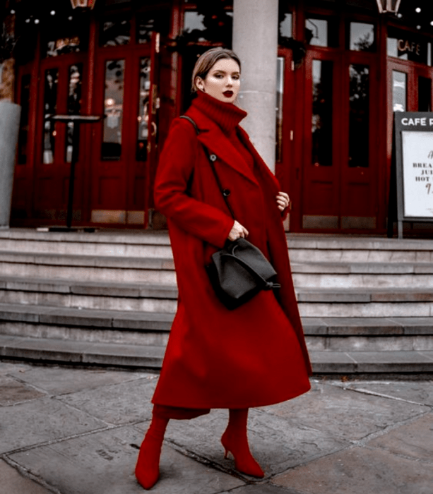 chica de cabello castaño usando un suéter de cuello alto rojo, abrigo largo rojo, pantalones rojos estilo culotte y botines negros de tacón, bolso negro de cuero crossbody bag