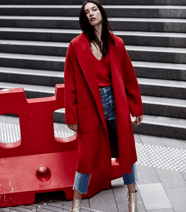 chica de cabello negro usando un top rojo de cuello en V, abrigo largo rojo, jeans ajustados, botines dorados de tacón