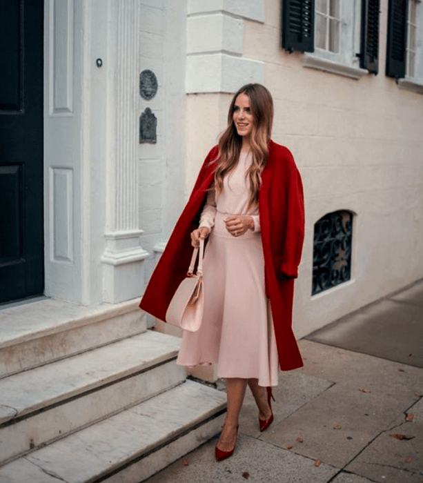 chica rubia usando un vestido rosa largo de manga larga y ajustado a la cintura, abrigo largo rojo, bolso de mano rosa y tacones rojos