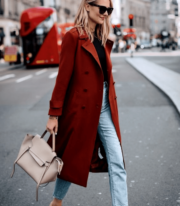 chica rubia usando un top negro de manga larga, abrigo rojo largo, jeans a la cintura, bolso de mano beige